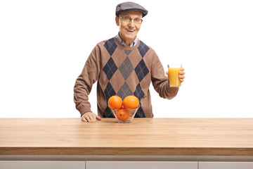 Senior man holding a glass of orange juice behind a wooden counter