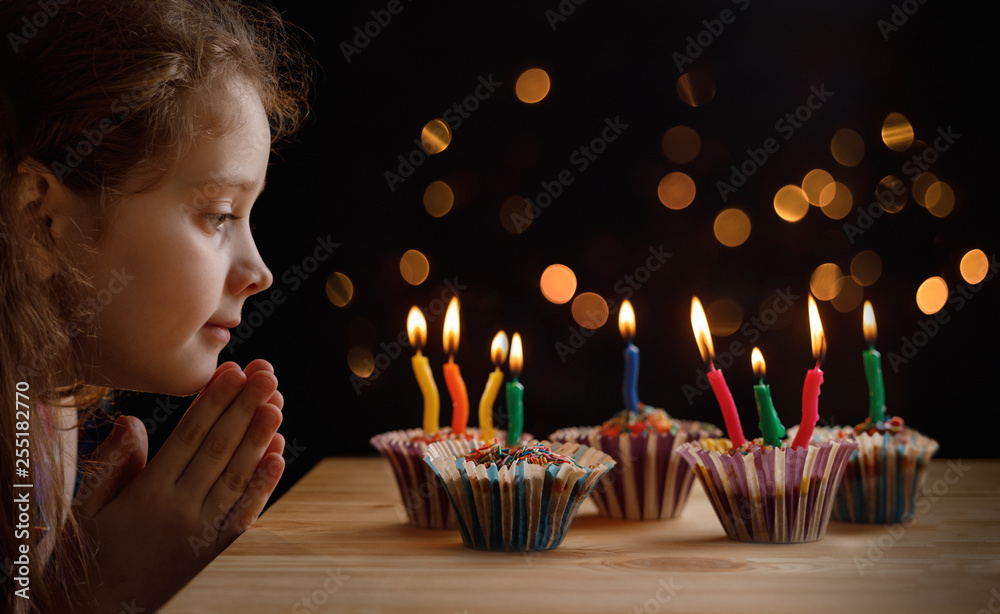 Cute little girl with party hat looking an the candles on birthday cakes. - obrazy, fototapety, plakaty 