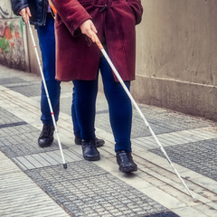 blind man and woman walking on the street using a white walking stick