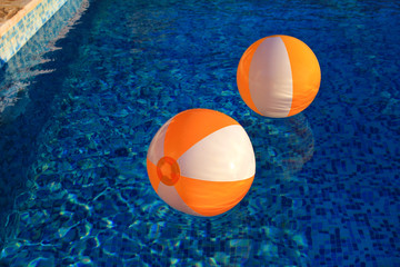 Wall Mural - Two rubber air yellow white inflatable balls and toy for swimming pool in transparent blue water. Multi-colored beach balls floating on water in blue swimming pool for concept relax holiday travel.