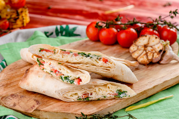 Burrito with meat and vegetables  on a wooden board on a red wooden background, decorated with napkins, chili pepper and cherry tomatoes. close up.