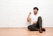 © luismolinero - Young man sitting on the floor pointing up and surprised