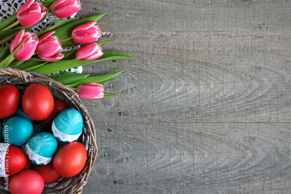 Wielkanocne tło z różowo-białymi tulipanami i kolorowymi pisankami w koszyku - obrazy, fototapety, plakaty 