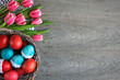 Wielkanocne tło z różowo-białymi tulipanami i kolorowymi pisankami w koszyku
