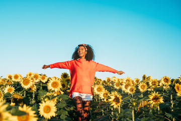 Happy young black woman walking in a sunflower field