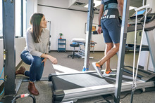 Physiotherapist Examining Patient Exercising On Treadmill In Clinic