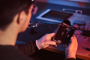 The technician carefully examines the integrity of the internal elements of the smartphone in a modern repair shop. Illumination with red and blue lights