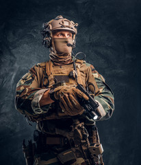 Wall Mural - Elite unit, special forces soldier in camouflage uniform holding a gun with a flashlight and looking sideways. Studio photo against a dark textured wall