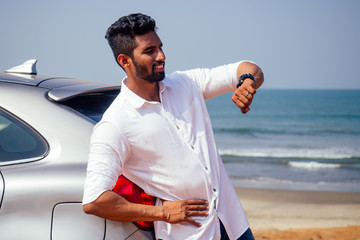 Wall Mural - handsome and successful indian man in a stylish well-dressed freelancer working with a laptop on the beach.freelance and remote work.businessman student in a summer cafe on the shore of india ocean