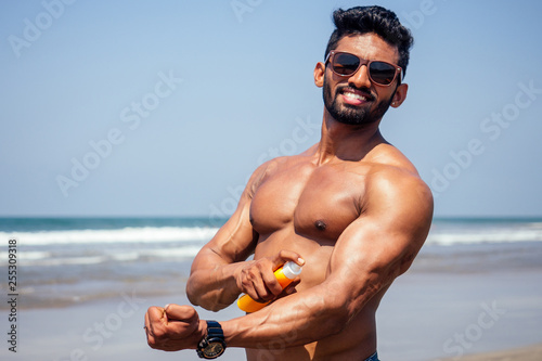 happy young african man on the beach.Handsome and confident Masculine hard  fitness bodybuilder with sixpack.India model male perfect abs,  shoulders,biceps, triceps,chest holding a bottle of sunscreen Stock Photo |  Adobe Stock