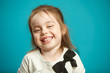 © Ilshat - Cute kid girl with a snide smile and low-key laughter stands on blue isolated background.