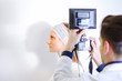 © GENETTICA - Doctor taking picture of young female patient before aesthetic treatment on white background.