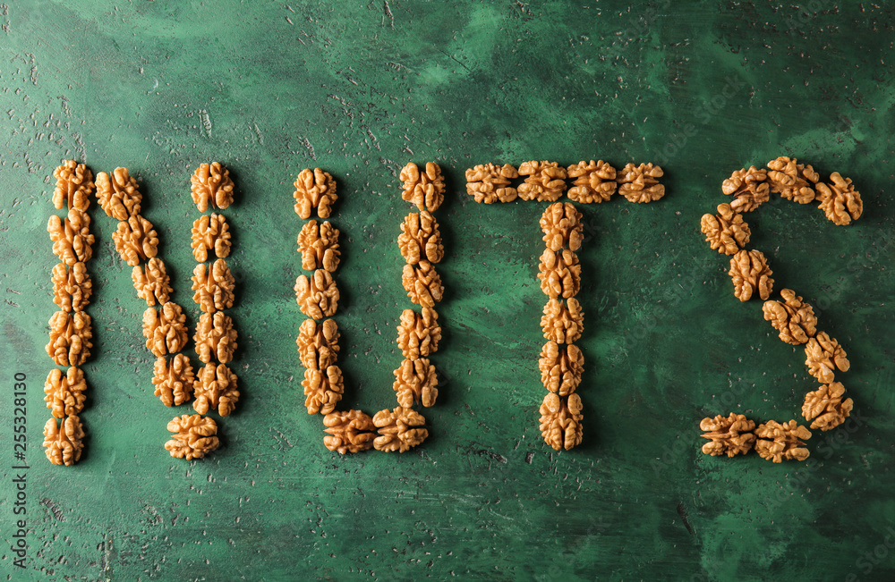 Word NUTS made of tasty shelled walnuts on color background