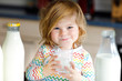 © Irina Schmidt - Adorable toddler girl drinking cow milk for breakfast. Cute baby daughter with lots of bottles. Healthy child having milk as health calcium source. Kid at home or nursery in the morning.
