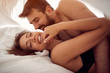 © luckybusiness - Smiling young couple lying and hugging in bed .