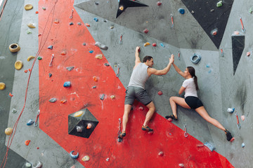 Young woman is happy to reach the top of the climbing wall. Black-haired woman made great effort and had success. The male instructor congratulating the young climber.