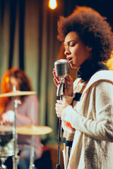 Wall Mural - Mixed race woman singing. In background band playing instruments. Home studio interior.