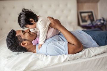 Wall Mural - positive Afro man touching his daughter's nose with his nise, funny game with a daddy,side view photo