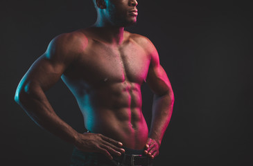 Close shot of athletic African well built man with six pack abs posing shirtless at studio over dark background.