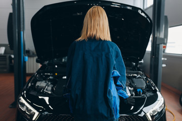 Wall Mural - blond woman standing in front of the car with opened hood. close up back view photo