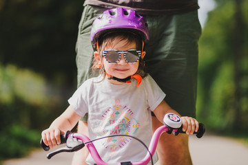 Wall Mural - father teaches little toddler daughter to ride a bike in the park