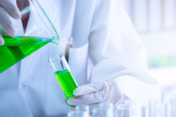 Green liquid substance was pouring into test tube by  scientist or chemist in science experiment  at laboratory . Research and scientific discovery concept.