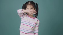 Portrait Of Little Asian Girl Say Good Bye And Waving Hand On The Green Background, Educational Concept For School Kids