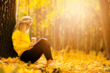 beautiful girl student reads the book alone in the autumn park in the rays of the warm sun. The concept of education, to do the lessons