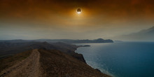 Total Solar Eclipse In Dark Red Sky Above Sea And Mountains