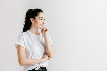 Happy woman standing and smiling isolated on gray studio background. Beautiful female half-length portrait. Young emotional woman. The human emotions, facial expression concept.