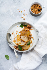 Wall Mural - Greek yogurt with caramelized pear, granola, nuts and melted sugar for a wholesome breakfast on a gray ceramic plate. Rustic style. Top view.
