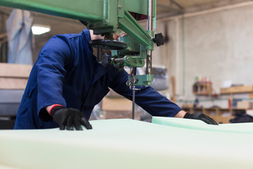 Wall Mural - Young man in a furniture factory is cutting the foam for the sofa