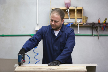 Wall Mural - Closeup of a young man in a furniture factory who puts together one part of the sofa with a stapler