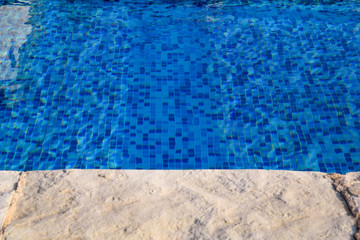 Blue ripped water in swimming pool in tropical resort with edge of pavement. Part of Swimming pool bottom background. Clear light blue pool water ripples with sun reflection. Surface of swimming pool.