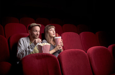 Wall Mural - Young cute couple sitting alone at red movie theatre and having fun