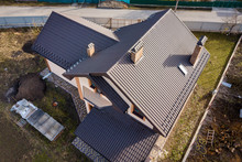 Aerial Top View Of Building Steep Shingle Roof, Brick Chimneys And Small Attic Window On House Top With Metal Tile Roof. Roofing, Repair And Renovation Work.