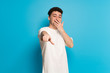 © luismolinero - Young man over blue background pointing with finger at someone and laughing