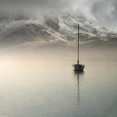 Canvas Print - Stunning landscape image of sailing yacht sitting still in calm lake water with mountain looming in background during Autumn Fall sunrise