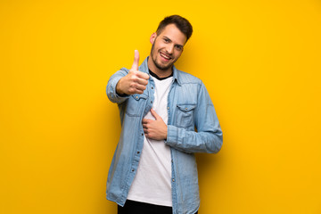 Handsome man over yellow wall with thumbs up because something good has happened