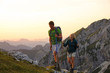 © helivideo - Hiker couple trekking up a grassy hill in the picturesque Alps at sunrise.