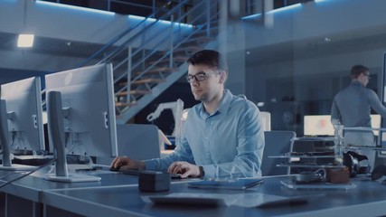 Electronics Development Engineer Sitting at His Desk Uses personal Computer for Programming. Team of Professionals Use Digital Whiteboard with CAD Software for the Modern Industrial Engineering Design