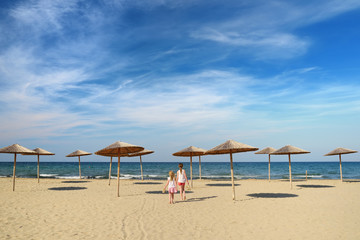 Two cute young sisters having fun on a sandy beach on warm and sunny summer day by the sea. Kids playing by the ocean.