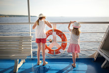 Adorable Young Girls Enjoying Ferry Ride Staring At The Sea On Sunset. Children Having Fun On Summer Family Vacation In Greece.