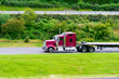 Dark red big rig bonnet classic American semi truck with empty flat bed semi trailer driving on highway to warehouse for pick up next load