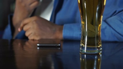 Wall Mural - African american man sitting in sports pub drinking beer and waiting for call