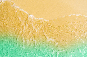 Top view of golden sand beach by the sea with emerald green sea water. Summer vacation on tropical paradise beach concept. Ripple of water splash on sandy beach. Summer vibes.