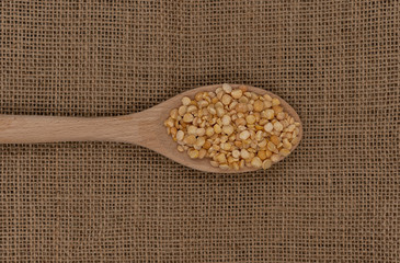 Wooden spoon with yellow  raw peas on a background of burlap texture