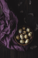 Wall Mural - Quail eggs in wooden bowl with feathers on dark wooden background.