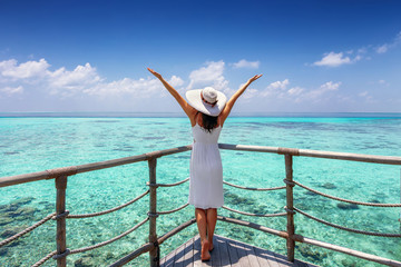 Travel concept: happy woman in white dress and sunhat enjoys her tropical vacation and feels the freedom