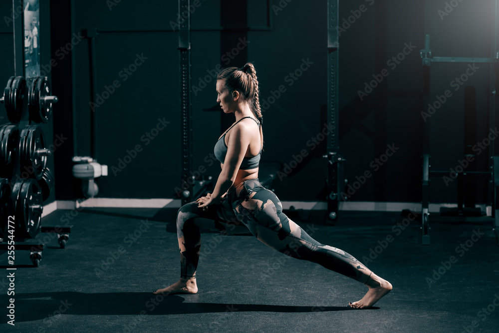 Young muscular Caucasian fit brunette stretching leg in gym. Side view ...